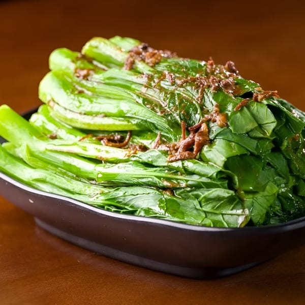 A black bowl filled with vibrant green Chinese vegetables, topped with a savory brown sauce.