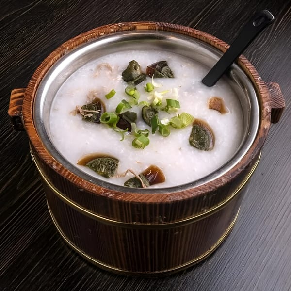 Chan Kee's century egg and shredded pork congee, garnished with green onions in a wooden bucket.
