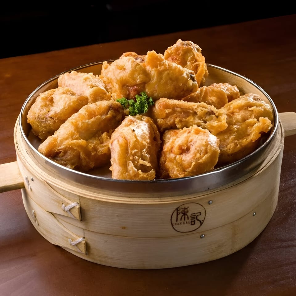 Golden-fried chicken pieces, garnished with parsley, served in a traditional Chan Kee bamboo steamer.