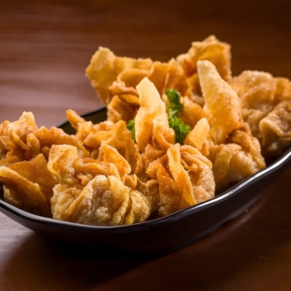 A black bowl filled with golden-brown fried wontons, garnished with a sprig of parsley.
